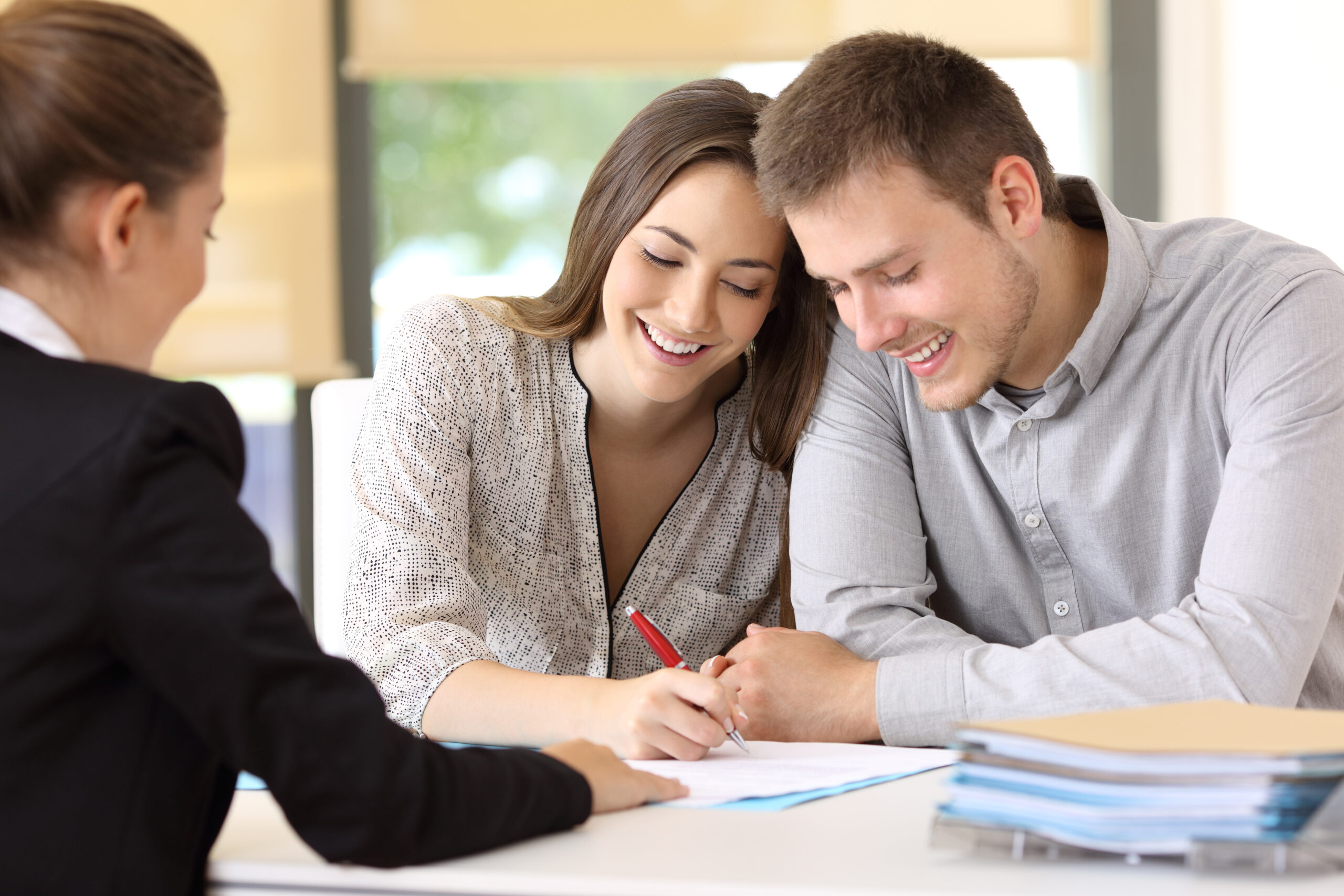 A happy young couple sign a document provided by a female solicitor.