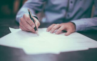 A closeup image of a man signing a will document.