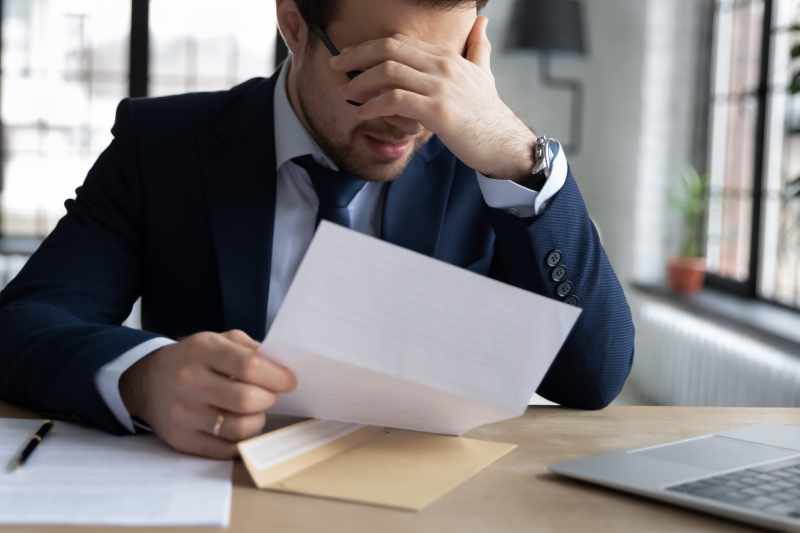 A distressed employee holds his head in his hands after reading a demotion notice.