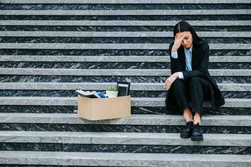 An employee sits outside of an office with a box of possessions after quitting her job.