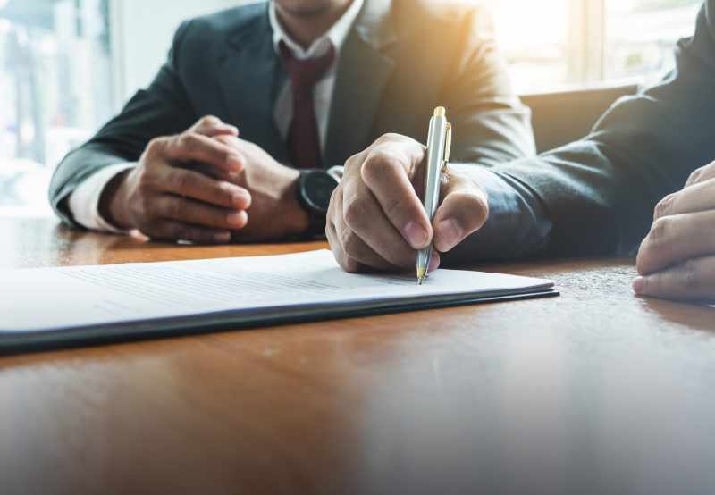 A closeup of two male business partners signing a legal document to proceed with an employment tribunal.