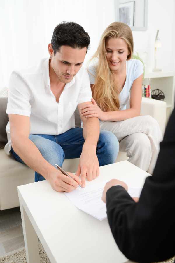 A young couple sign a document to appoint an attorney during a consultation with a solicitor.