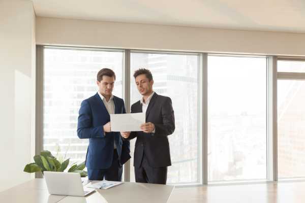 Two male business partners discuss property development projects in a modern office.