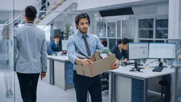 A dismissed male employee walks through the office with a box of his personal possessions.