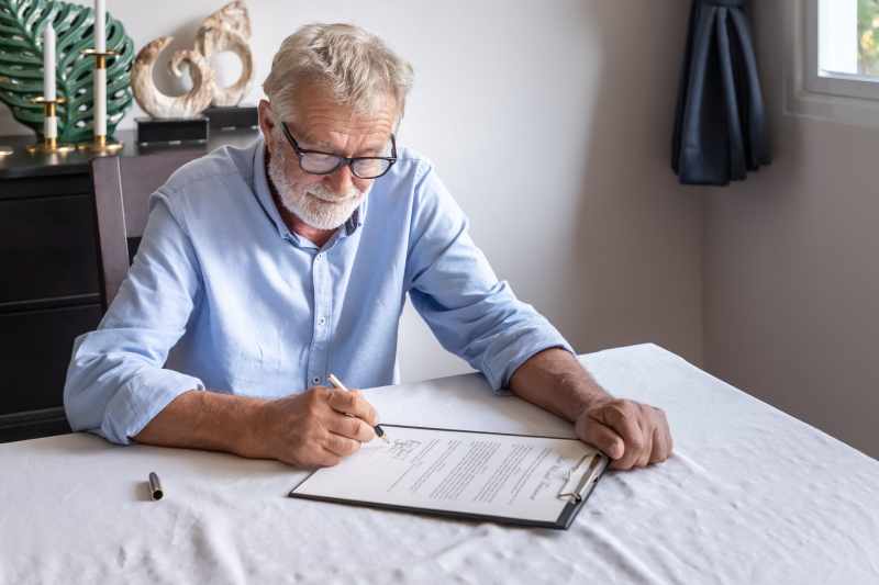 A smiling elderly man reviews and signs his will.