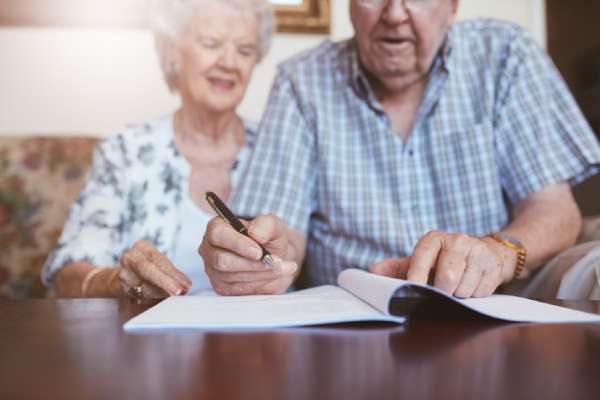 A smiling elderly couple sit on the sofa and read through their will documents