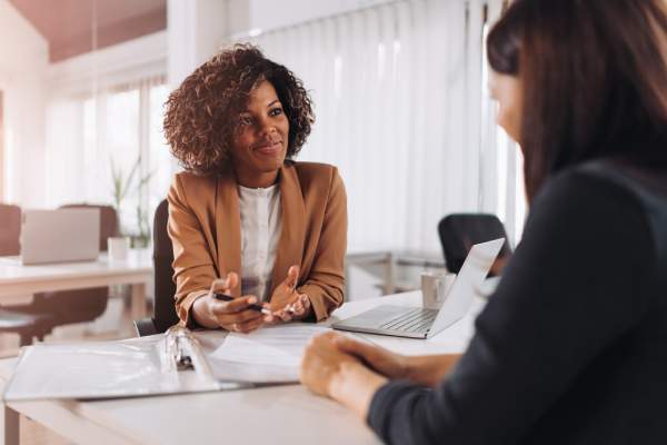 A young woman is interviewed by a cheerful female employee in a modern office.