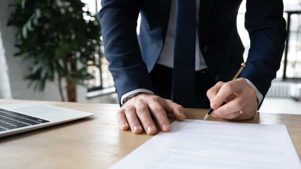 A closeup image of a man signing an employment contract in a modern office setting.